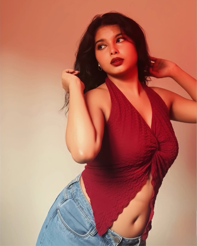 Diya Celebrity Escorts in Indore posing confidently in a red top and white skirt against a textured wall