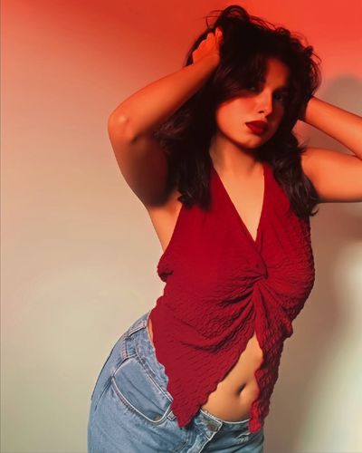 Portrait of Diya Celebrity Escorts in Indore standing near a wall, wearing a stylish red blouse and earrings