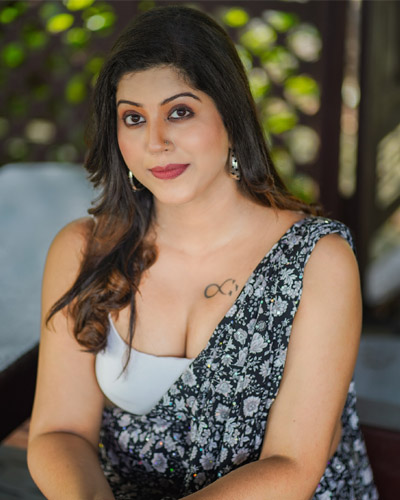 Woman seated outdoors wearing a patterned sleeveless outfit.