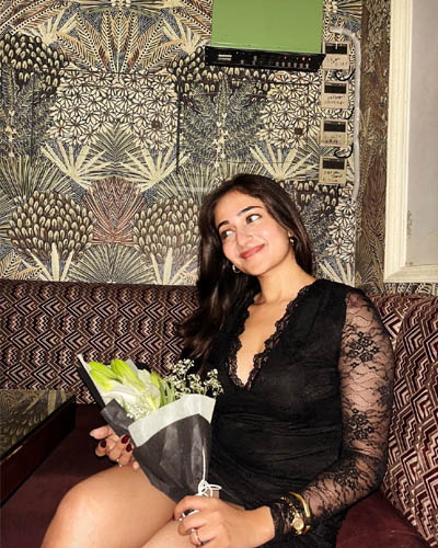 Elegant Riya Super Hot Escorts in Indore posing in a restaurant, dressed in a stylish black lace outfit with a drink on the table.