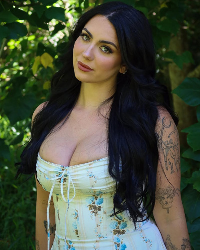 Zoya Foreigner Escorts in Indore looking at the camera in a white floral outfit, surrounded by purple petals